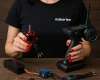 Siyah "makerion" tişört giyen, kırmızı ojeli kadın, ahşap masa üzerinde RC (Radyo Kontrollü) sistem donanımlarıyla çalışıyor; bir elde fırçasız motor, diğer elde 2.4GHz RC verici bulunuyor.