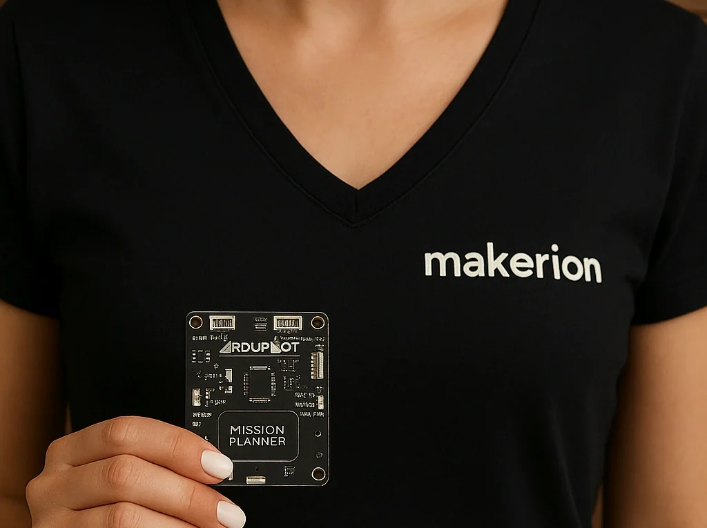 Makerion logolu siyah V yaka tişört giymiş, beyaz ojeli parmaklarıyla elektronik kontrol modülü tutan kadın; koyu ahşap fon önünde, yüzü kadraj dışında bırakılmış.